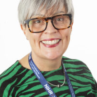 Sam Debbage smiling, wearing glasses and a green and black zebra-patterned top